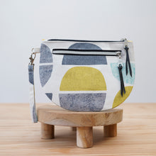 Load image into Gallery viewer, Fabric pouch with geometric pattern on a wooden stand against a light Brooke Wristlet Sewing Pattern PDF background