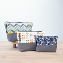 Load image into Gallery viewer, Three patterned pouches with gray bases on a light wooden surface. Cecily Zipper Pouch Sewing Pattern PDF