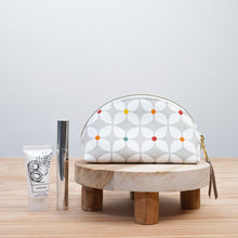 Load image into Gallery viewer, Cosmetic bag with colorful pattern on a wooden stand, accompanied by skincare products. Seren Dumpling Sewing Pattern PDF