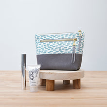 Load image into Gallery viewer, Cosmetic bag with a patterned top half and solid gray bottom half, accompanied by a bottle and tube on a wooden surface. Ayla Zipper Pouch Sewing Pattern PDF
