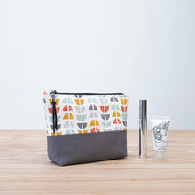 Load image into Gallery viewer, Patterned pouch with a gray bottom on a wooden surface, accompanied by a bottle and a tube. Cecily Zipper Pouch Sewing Pattern PDF
