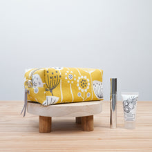 Load image into Gallery viewer, Yellow floral-patterned pouch on a wooden stool with a silver bottle and white tube on a light wood surface. Demi Boxy Bag Sewing Pattern PDF
