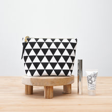 Load image into Gallery viewer, Black and white geometric patterned pouch on a wooden stool with a small bottle and tube on a light wood surface. Verity Zipper Pouch Sewing Pattern PDF

